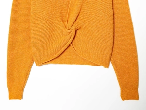 Detail view of the vertical rib-knit texture and twist knot design on the orange sweater