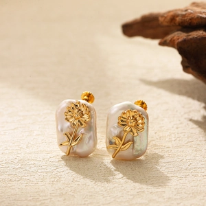 Macro detail of baroque pearl earrings with gold flower charms on a textured surface