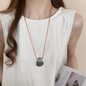 Detail of silver shell pendant on a thin orange cord worn with a white linen top