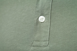 Détail macro d'un polo en coton de haute qualité montrant le bouton et les coutures vert haricot