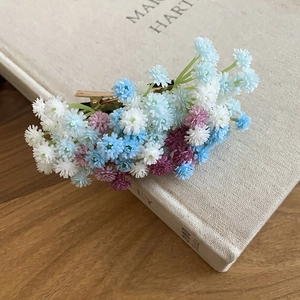 Détail de grappes de fleurs artificielles bleu ciel et violettes sur une pince dorée