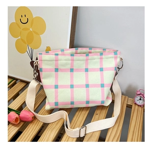 Detail view of canvas crossbody bag with pink and green plaid pattern on a wooden bench