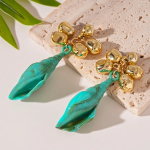 Detail of teal resin shell drop earring with golden beads on a stone platform