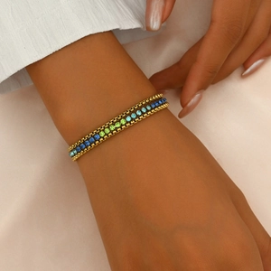Detailed view of three layered gold chains with sapphire and emerald crystals on wrist