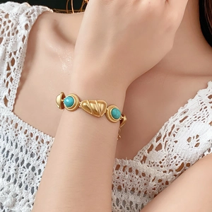 Gros plan d'un bracelet doré vintage avec pierres vertes porté sur une manche en dentelle