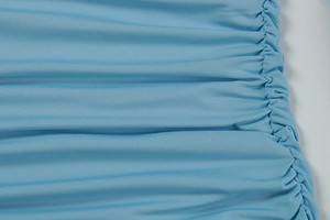 Macro detail of light blue ruched fabric showing knit texture and pleated craftsmanship