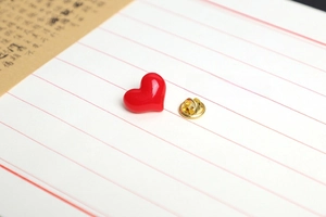 Macro shot of a red heart-shaped enamel pin with a gold butterfly clutch on paper