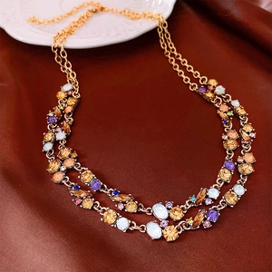 Close-up of double-layer gold necklace with colorful crystals on soft silk fabric