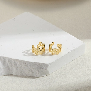 Detailed view of hollow gold-plated leaf ear cuffs on a textured stone display