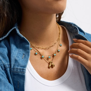 Dettaglio collana a strati dorata con fiore turchese e pendente lettera A su modella