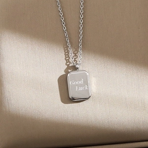 Minimalist silver necklace with Good Luck engraved pendant on beige fabric background