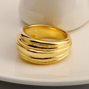 Close-up of 18K gold plated wide band ring with horizontal ribbed texture on a ceramic dish