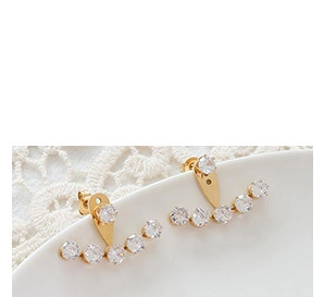 Macro view of gold-plated ear cuffs with curved zircon stone inlay on white lace decor