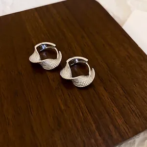 Minimalist twisted silver hoop earrings with textured finish on a dark wooden display