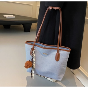 Detail of blue textured fabric tote bag with brown leather handles and teddy bear charm