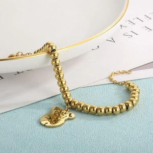 Detailed shot of 18K gold plated beaded bracelet with cute bear charm on ceramic plate