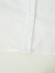 Detailed close-up of white linen shirt hem and texture with a round four-hole button
