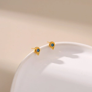 Detailed close-up of 18K gold teardrop earrings with turquoise stone on white ceramic tray