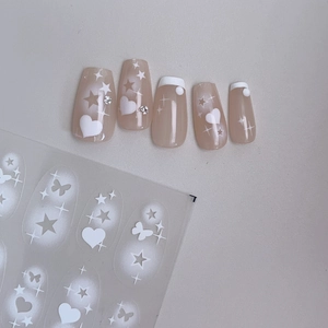 Detail of pink press-on nails featuring white heart and star patterns with small rhinestones
