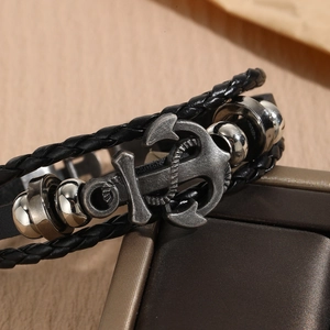 Macro detail of a vintage black braided leather bracelet with a silver anchor pendant