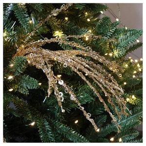 Close-up of golden sequin branch ornaments on a Christmas tree with warm white lights