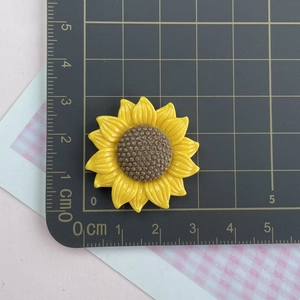 Detailed size view of a yellow resin sunflower accessory on a metric measuring ruler