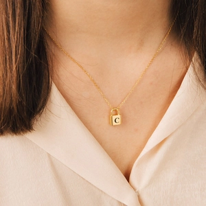 Close-up of a gold padlock necklace featuring an engraved letter C pendant on a model