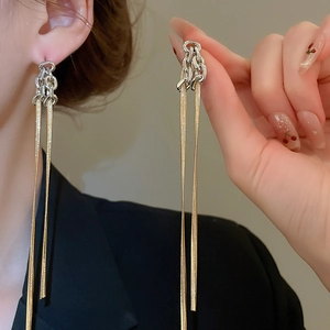 Détail de boucles d'oreilles à pompons avec nœud argenté et chaînes serpent dorées