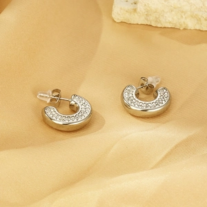 Macro view of silver C-shaped earrings with pave-set zircons on yellow satin background