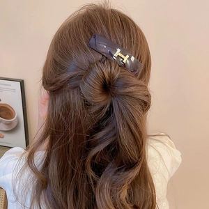 Detail of a vintage acrylic oval hair clip with a gold H letter on long brown hair