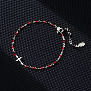 Detailed macro view of stainless steel cross bracelet with small red beads and lobster clasp
