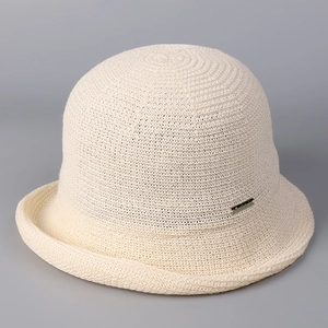 Detailed close-up of knit texture and golden metal logo on off-white linen cloche hat