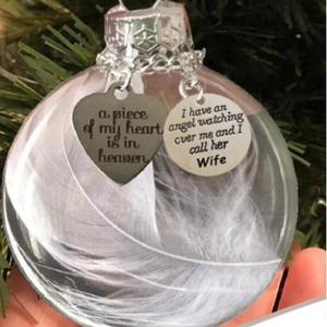 Memorial Christmas feather ornament with silver heart tag held against a pine tree