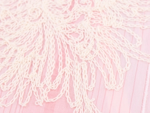 Detailansicht von rosa Stoff mit aufwendiger weißer Blumenspitze und Häkelstricktextur