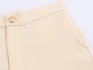 Close-up of beige tailored trousers featuring a textured gold button and side pocket