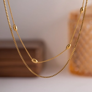 Elegant gold double-layered necklace featuring box chain and oval bead pendants