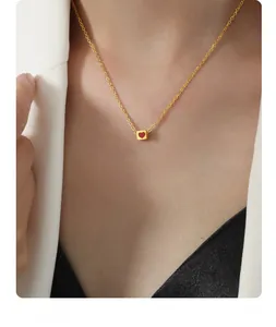 Detail of a minimalist gold necklace with a red heart cubic pendant on a model