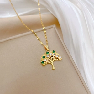 Elegant gold life tree necklace with green and white crystals on soft fabric background