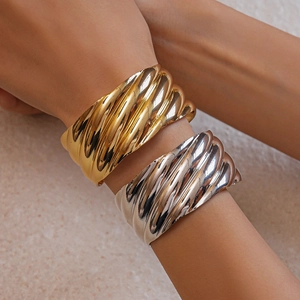 Close-up of gold and silver metallic wavy spiral open bracelets worn on a wrist
