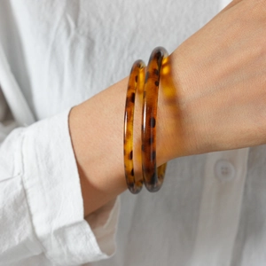 Detail von Acryl-Armreifen mit Schildpattmuster am Handgelenk eines Modells mit Leinenhemd