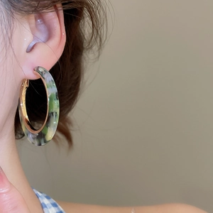 Close-up of a model wearing green marble-patterned acetate hoop earrings with gold metal
