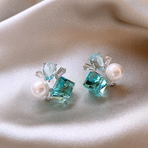 Dettaglio di orecchini con zircone blu e perla su elegante sfondo di seta color champagne