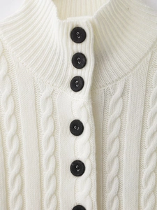 Close-up of white cable knit cardigan featuring black buttons and textured rib collar