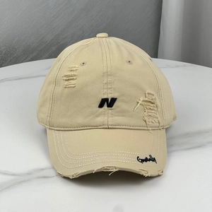 Close-up of distressed beige baseball cap with black letter N embroidery and torn brim detail
