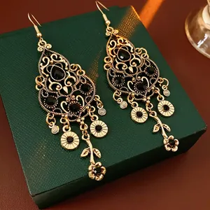 Vintage gold-tone floral tassel earrings with black rhinestones on a green jewelry box