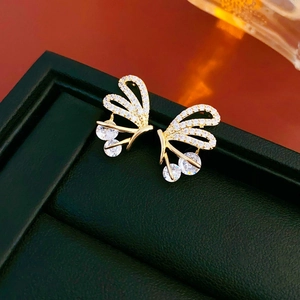 Macro shot of gold plated hollow butterfly earrings with zircon stones on green leather