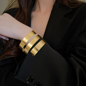Dettaglio di un ampio bracciale a spirale dorato indossato sopra una manica nera