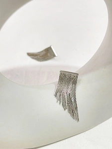 Detail of silver metal tassel chain earrings on a white minimalist geometric display