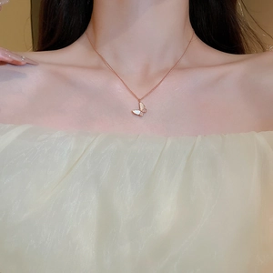 Detailed view of rose gold butterfly pendant with white shell wings on a model's neck