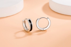 Close-up of minimalist silver hoop earrings with black enamel inlay on a white stand